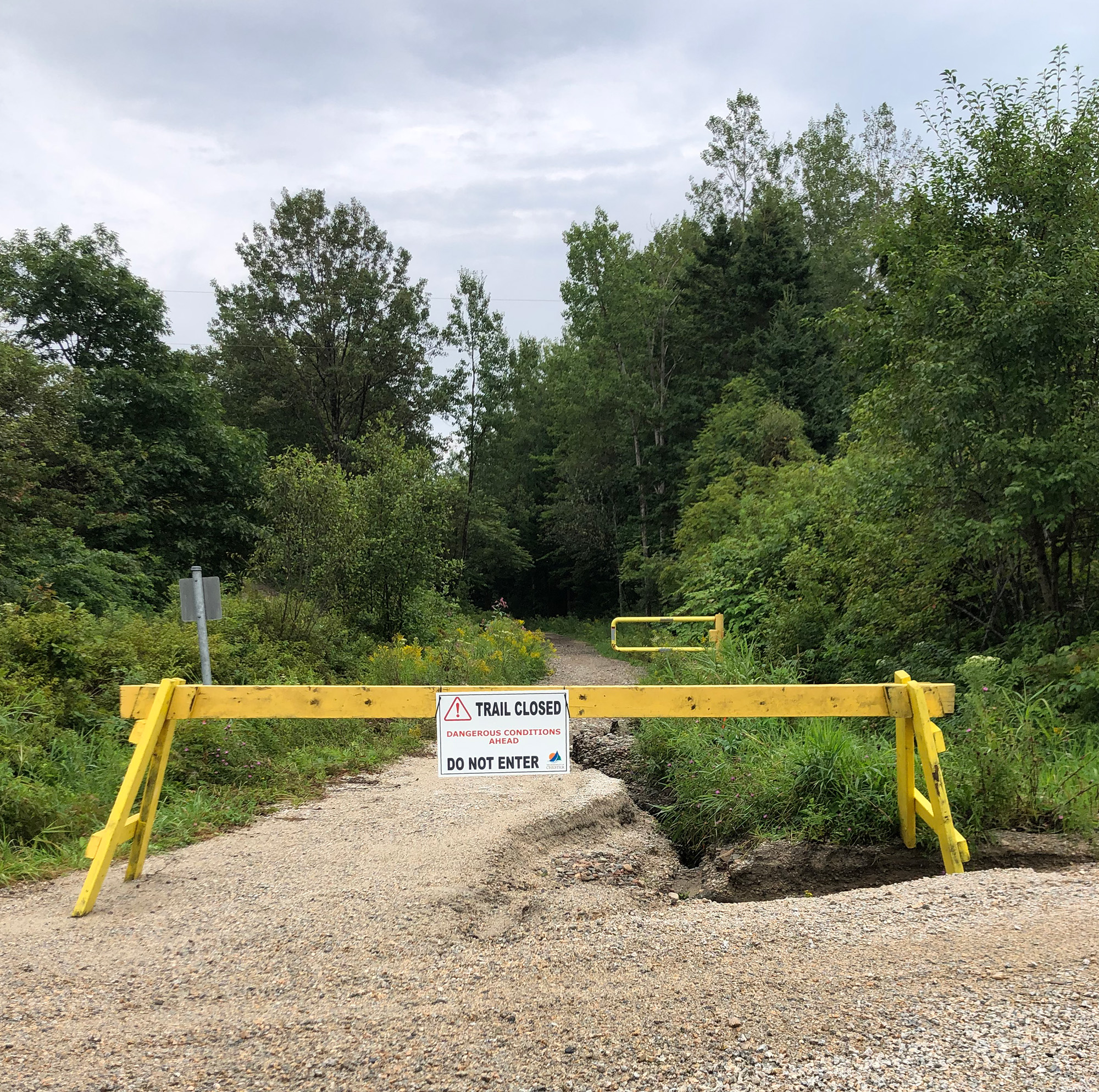 washed out trail blocked off with a barricade and sign that reads, "trail closed".