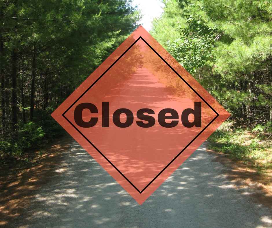 orange closed sign overlaying a forested trail