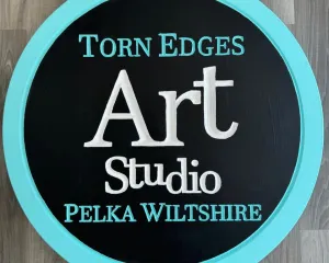 photo of Torn Edges Art Studio business. Round with black background and blue border.