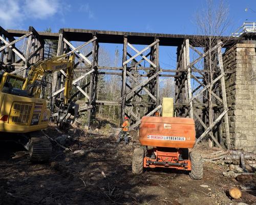 Lift and excavator beside wooden train bridge trestles