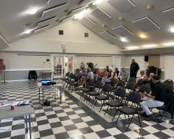Room with rows of chairs and people looking ahead at a presenter that is out of shot